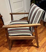 Side profile of vintage teak wood side chair with striped upholstery and angled armrests.