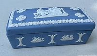 Photo of a vintage rectangular Wedgwood blue jasperware box with white bas-relief classical decoration on the lid and sides, shown closed.