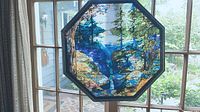 Octagonal stained glass panel showing a canyon landscape with blue river, green trees, and rocky cliffs, framed in dark wood hung in window.