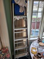 Full view of silver aluminum ladder with several wide steps placed indoors near windows and furniture.