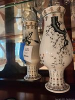 Pair of Asian-themed porcelain vases with branch and flower designs shown from an angled front view on a glass shelf.