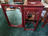 Photo showing cherry wood square accent table with geometric cutouts and matching framed mirror against a carpeted floor.