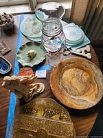 Wide angle shot showing entire lot on wood table by window, including all platters, glass vase, couple statue and decorative items