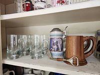 Middle shelf displaying assortment of glass mugs, ceramic, and wooden steins