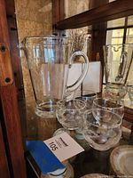 Clear glass pitcher with handle and four stemless frosted etched glasses displayed on a shelf with wood and marble background
