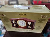 Photo of the mantel clock's box showing the product image, brand Gold Label Collection, and model Symphony Surprise Angel Orchestra. Box details visible including features and specifications on the sides.