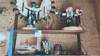 Shelf with two large Native American figurines showing detailed feather headdresses and shields, smaller figurine, and painted plate.