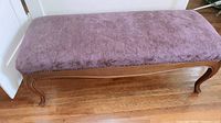 Full side view of the purple upholstered wooden seating bench on hardwood floor near white door.
