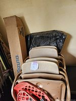 Side view of stacked beige and one red vintage folding chairs, showing metal frames and padded seats and backs.