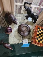 Glass tabletop with multiple walnut wood carvings and a wooden chess board arranged on a stone slab base