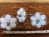 Three opal glass floral tie backs shown on wooden surface with measuring tape showing size approx 3 inches diameter each