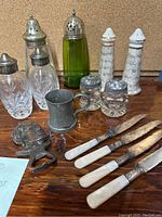 Overall view of antique shakers, cutlery, metal cup, and bottle opener on wooden surface