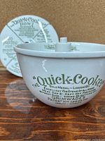 Side view of white ceramic Quick Cooker bowl with printed green text on front showing 'Quick Cooker Bowl' instructions and patent info.