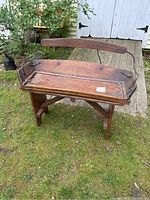 Overall view of the antique horse buggy bench showing wood seat and iron sides, with a wooden backrest, photographed outdoors on grass.