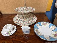 Photo showing the Royal Winton two-tiered cake stand with floral motif, Royal Copenhagen toothpick holder, Noritake pedestal dish, and Shelley bowl with plate.