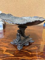 Side view of pedestal dish showing detailed base with horn and seated female figure