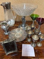 Full lot display showing crystal compote, silver plated items, colored glass goblets and frame.