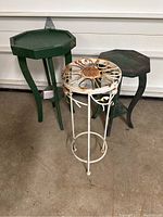 Three plant stands together, two green wooden sets and one rusted iron stand