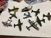 Photo showing a lot of nine model aircraft including military planes and a helicopter on a white surface.