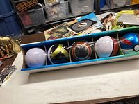 Set of five Poké Balls in a box: white Poké Ball, black and yellow Ultra Ball, red and white Great Ball, white Poké Ball, and blue and purple Master Ball variant.
