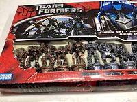 Box front showing Transformers branding and some chess pieces inside visible through window, box is damaged.