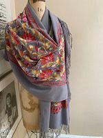 Full view of the periwinkle cashmere shawl displayed on a dress form showing floral embroidery and fringed ends.