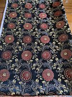 Close-up image of the black fabric with red floral details and gold metallic foliage pattern, showing texture and color.