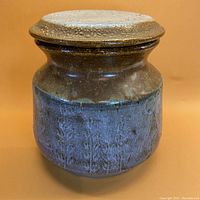 Front view of the large ceramic vessel showing grey blue glaze and sandy textured lid