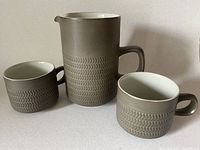Pitcher and two cups in olive green with raised chevron detail showing overall set