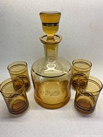 Full view of amber decanter with stopper and four matching glasses arranged around it, showing gold and chocolate stripes and etched details.