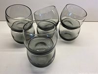 Eight smoky grey roly poly glasses arranged with some stacked and others near flat on white surface to show form and color.