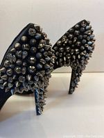 Close-up of black suede heel showing dense chrome spikes and charcoal crystals on the back and heel