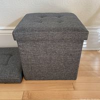 Side view of one grey speckled folding storage ottoman, showing tufted lid and fabric texture.