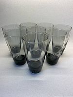 Front angled view of 8 smoky grey tumblers grouped closely on light surface showing color, size, and shape.