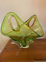 Full view of the lime green blown glass vessel with cinnamon handles and clear glass legs on wooden surface.