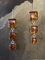 Full view of both earrings showing three square amber resin segments each with preserved flowers inside and sterling silver framing.