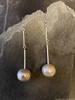 Front view of both earrings showing long posts and spherical dangles with etched design on a dark background.
