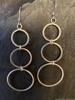 Pair of vintage sterling silver earrings with three circular linked rings each, hanging vertically with hook fasteners on black background.