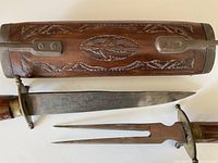 Photo of hand carved wooden sheath and knife blade and fork blade visible outside sheath.