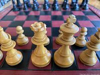 Close-up photo of natural wooden chess pieces including king, queen, bishop, and pawns on leather board with black and red squares.