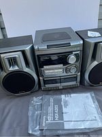 Full view of the Aiwa CX-NA202 compact stereo system with both speakers and manual on the table.