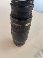 Close-up of Canon EF 100-300mm f/5.6 zoom lens showing focal length range and Promaster filter labeled Japan.