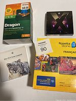 Four software boxes including Dragon NaturallySpeaking 10, Mac OS X Snow Leopard disc and boxed Mac OS X, Rosetta Stone French edition.