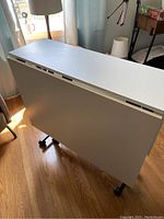 Photo of the table folded flat showing white top and wheels