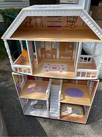 Full front view of wooden dollhouse showing three levels, interior wall decals, staircase, and open front design.