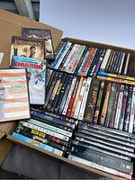 Photo of multiple DVDs including The Lord of the Rings trilogy box set, How to Train Your Dragon, Juno, and a large assortment of other DVD titles arranged in a box.