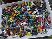 Top view of a large variety of Hot Wheels cars in a white bin