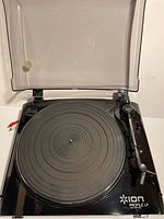 Front view of the Ion Profile LP turntable showing the platter and dust cover, with hinges attached but broken.