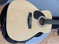 Full front view of acoustic guitar body showing natural wood top and black pickguard.