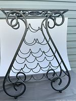 Front view of the ornate metal wine rack showing curved bottle holders and base details